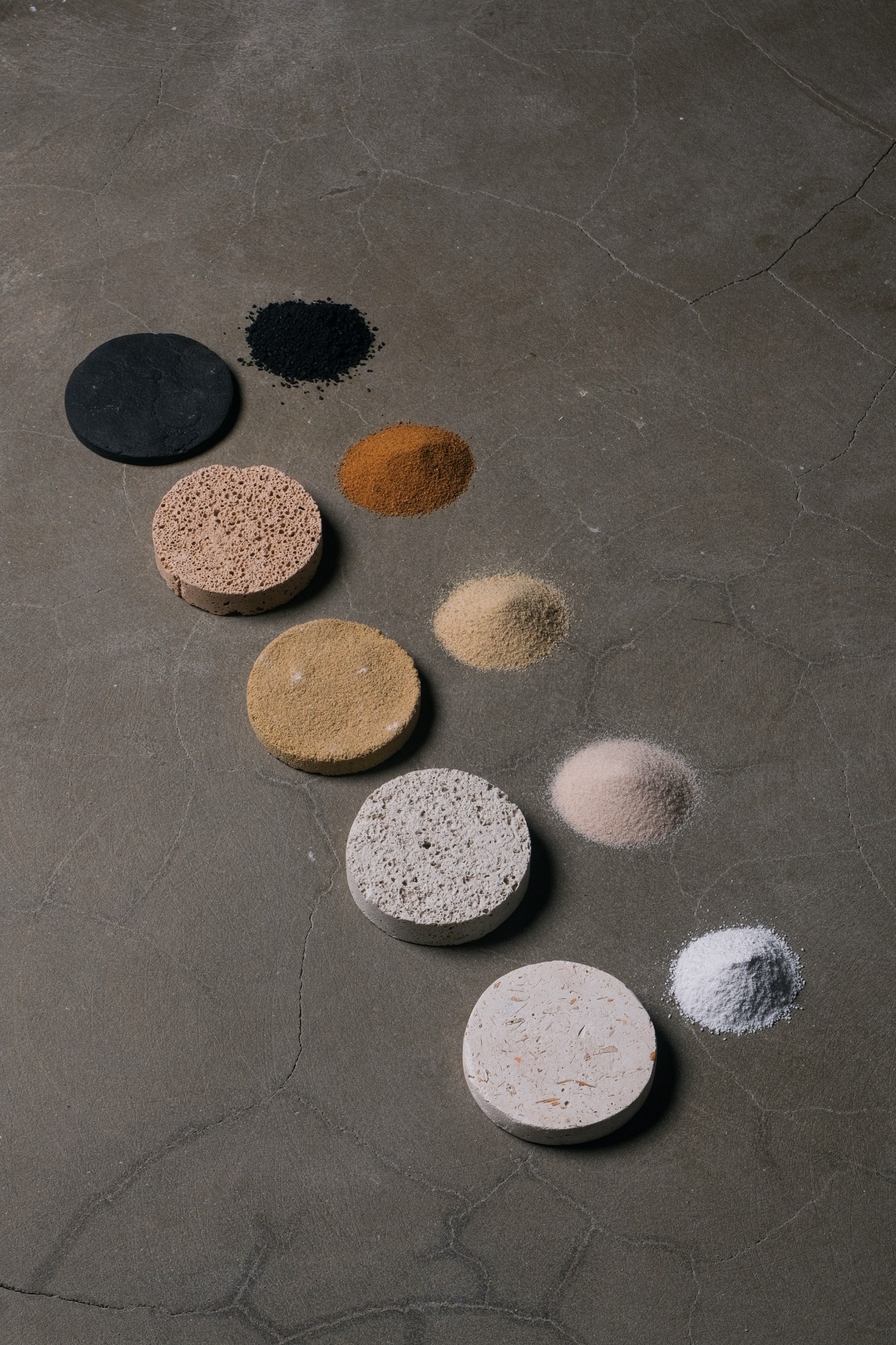 Composite material samples and raw mineral powders arranged on a dark surface